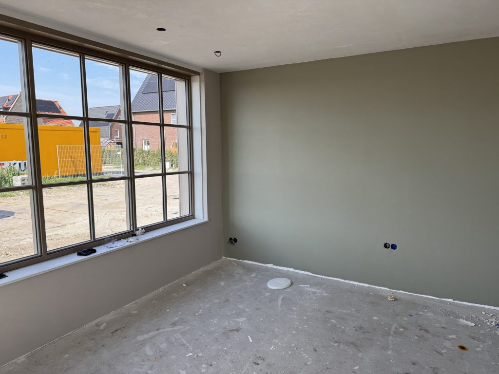 Nieuwbouwkamer met een egaal gesausde grijsgroene wand en een groot raam