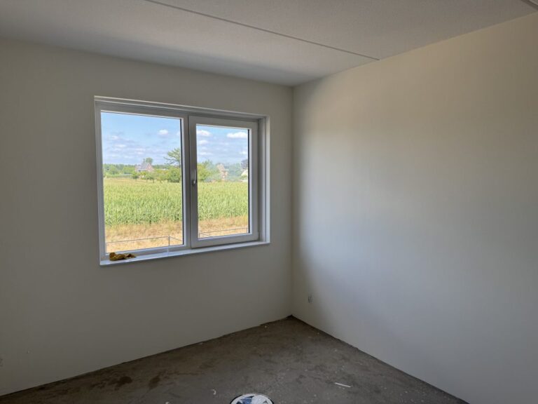 Lege nieuwbouwkamer met gladde, lichte wanden en een raam met uitzicht over het land