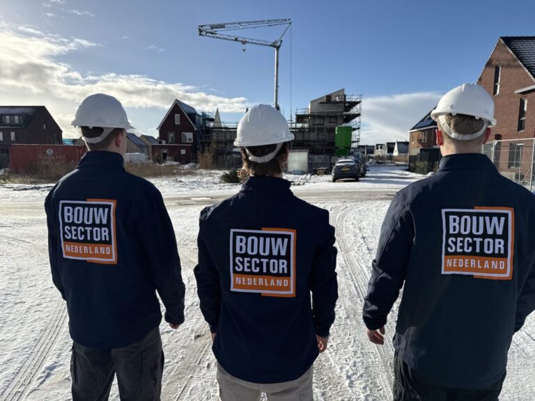 Drie vakmensen van Bouwsector Nederland in bedrijfsjas en met bouwhelm bij een nieuwbouwwijk